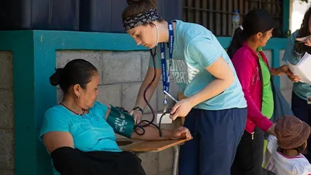 Nursing student taking woman's blood pressure outside.