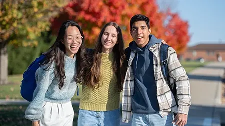 Three students smiling with arms around each other.