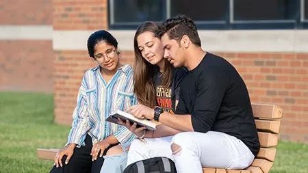 Three students sitting on bench reading Bible.