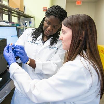 One white female and one black female wearing white lab coats looking at a test tube